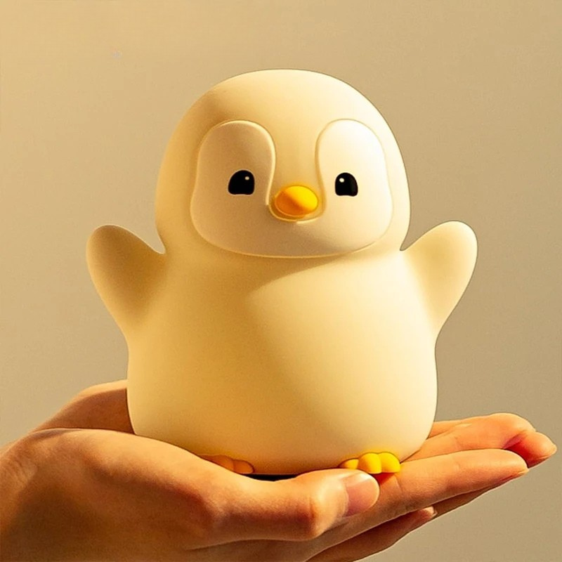 Veilleuse pingouin blanc et jaune en silicone souple Pingo-Doux lumineuse sur un lit - Rituel Dodo.
